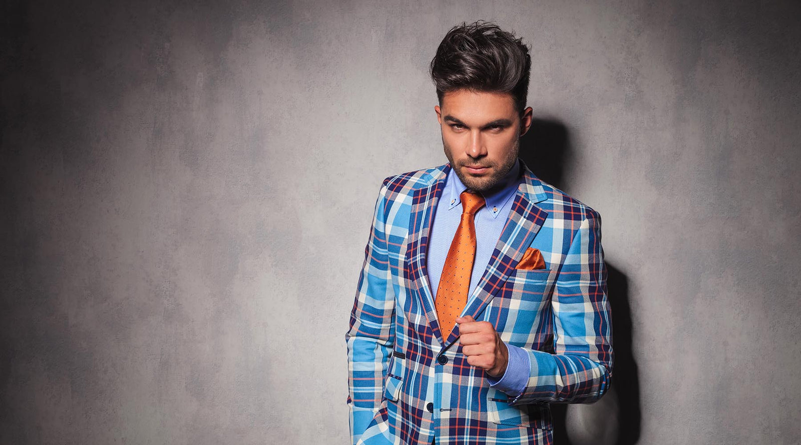 handsome young man wearing orange tie and pocket square with teal white and orange plaid suit